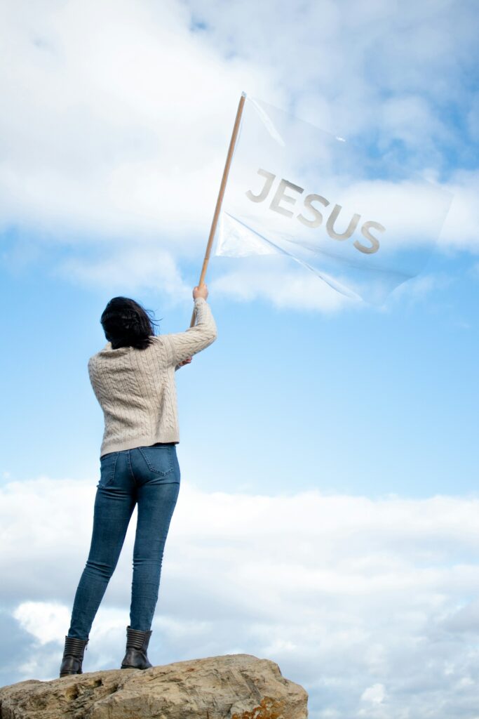 woman in white shirt blue denim jeans holding jesus flag
