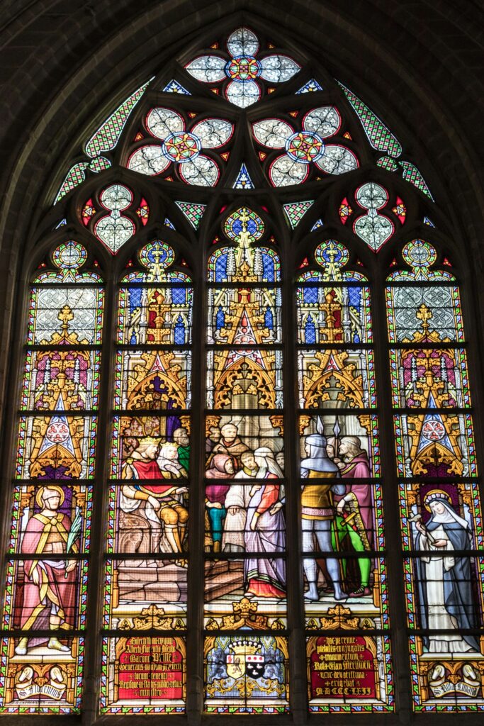 a large stained glass window in a church pierre goiffon unsplash